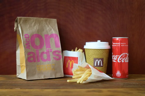 맥도날드는 종이 봉투와 코카콜라 캔을 나무 테이블에 감자 튀김을 가져 가라. — 스톡 사진