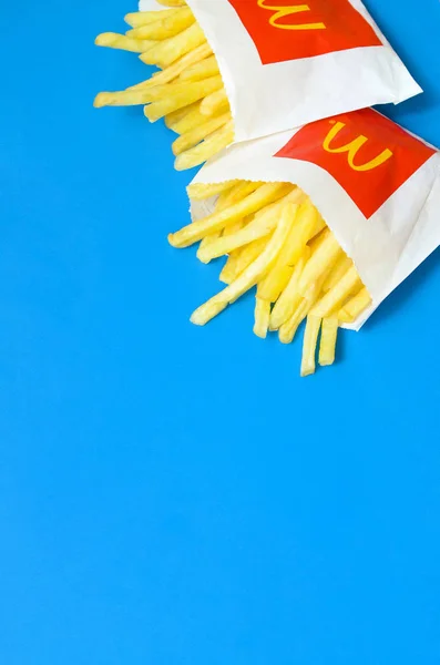 Papas fritas McDonald 's en una pequeña bolsa de papel sobre fondo azul brillante —  Fotos de Stock
