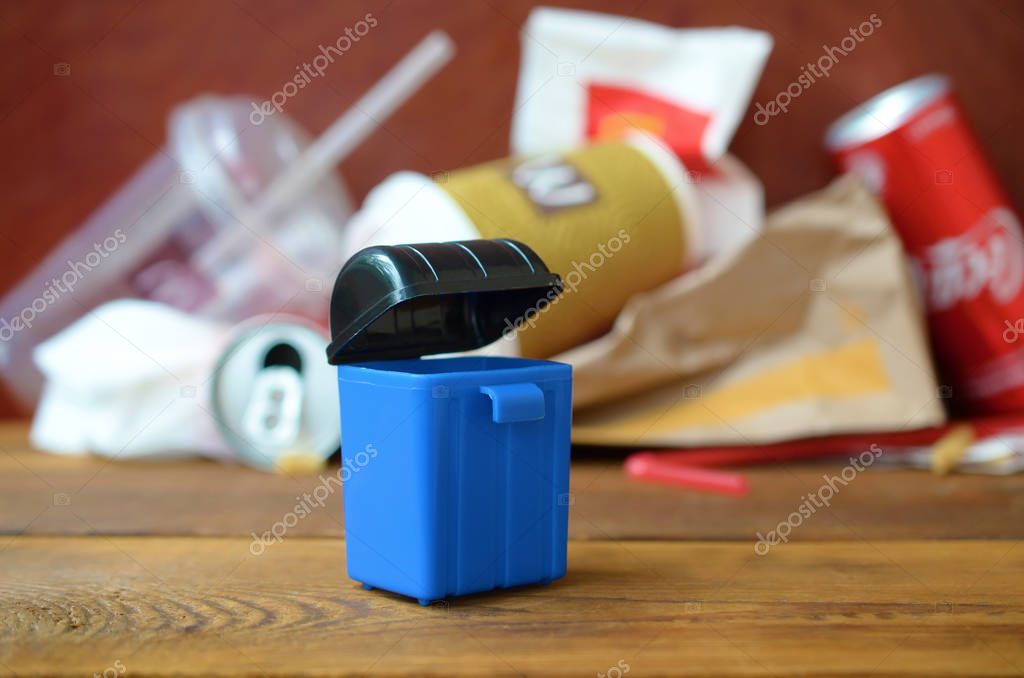 KHARKIV, UKRAINE - AUGUST 1, 2019: Toy garbage bin and McDonald's disposable trash on dark brown wooden background as a symbol of a need for environmental, obesity and health awareness