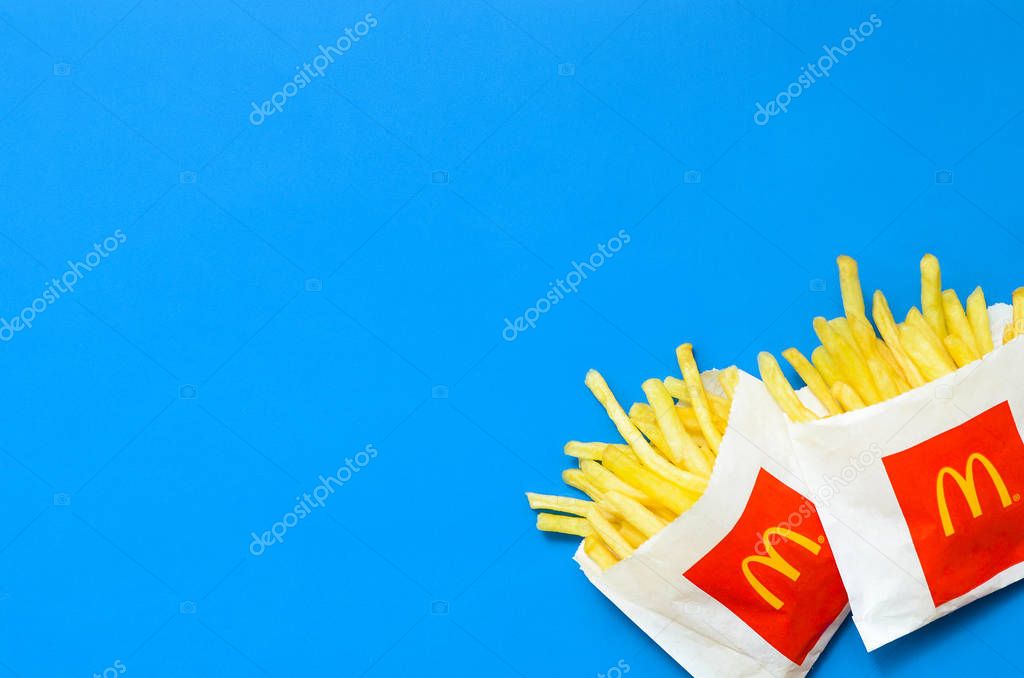 KHARKIV, UKRAINE - AUGUST 1, 2019: McDonald's French fries in small paperbag on bright blue background. McDonald's Corporation is the world's largest and famous fast food restaurant