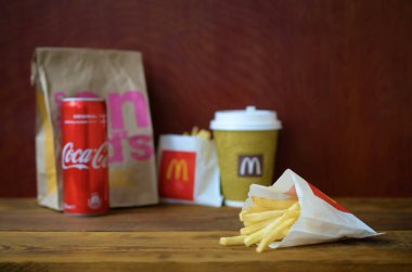 Mcdonald's ahşap masa üzerinde coca cola kutu ile kağıt torba ve patates kızartması götürmek