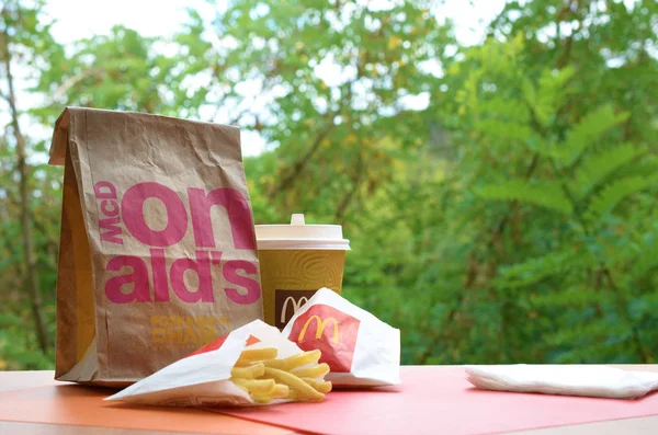 McDonald's take away paper bag and junk food on wooden table outdoors — Stock Photo, Image