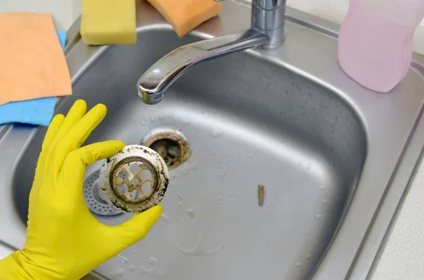 Cleaner in rubber gloves shows waste in the plughole protector of a kitchen sink — Stock Photo, Image