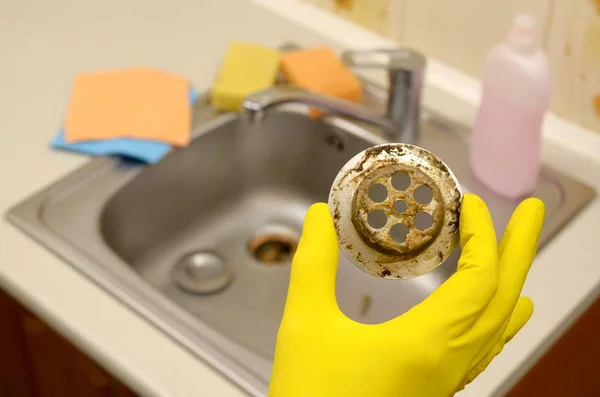 Nettoyant dans des gants en caoutchouc montre les déchets dans le protecteur plughole d'un évier de cuisine — Photo