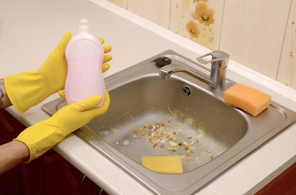 Cleaner shows liquid cleanser detergent bottle at dirty kitchen sink with food particles before the cleaning — Stock Photo, Image