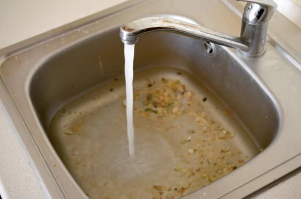 Stainless steel sink plug hole close up full of water and particles of food — Stock Photo, Image