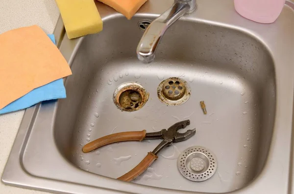 Pliers inside the silvery kitchen sink with a disassembled protective filter — Stock Photo, Image