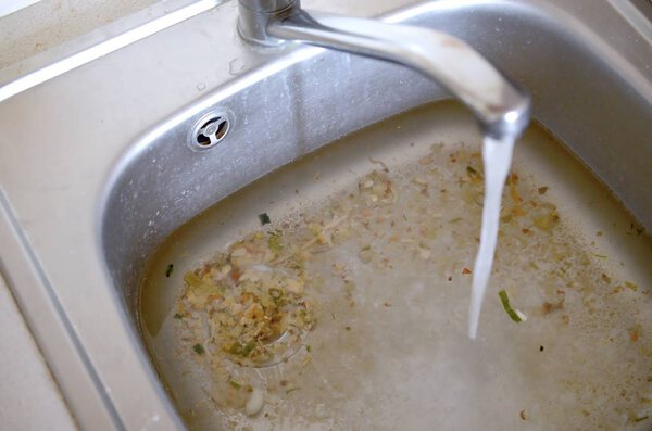 Stainless steel sink plug hole close up full of water and particles of food