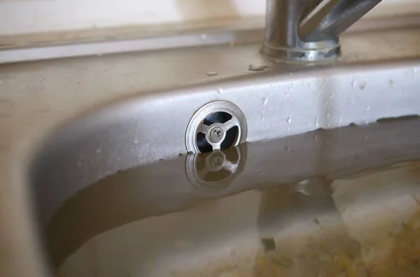 Stainless steel sink plug hole close up full of water and particles of food — Stock Photo, Image