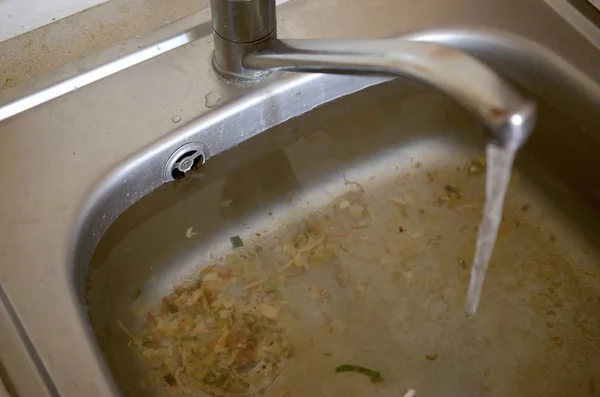 Stainless steel sink plug hole close up full of water and particles of food — Stock Photo, Image