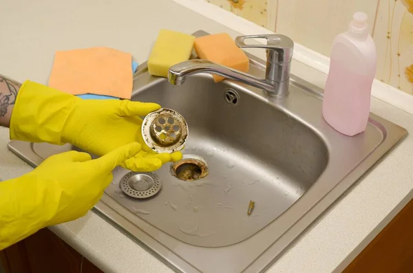 Detergente in guanti di gomma mostra i rifiuti nel protettore dello scarico di un lavello da cucina — Foto Stock