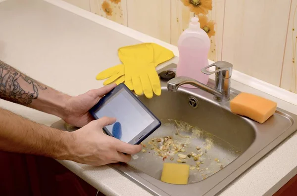 The landlord uses the tablet to call a cleaner in order to clean the clogged kitchen sink — Stock Photo, Image