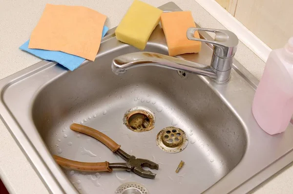 Pliers inside the silvery kitchen sink with a disassembled protective filter — Stock Photo, Image