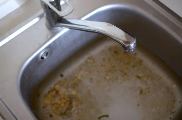 Stainless steel sink plug hole close up full of water and particles of food — Stock Photo, Image