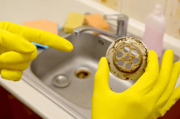 Nettoyant dans des gants en caoutchouc montre les déchets dans le protecteur plughole d'un évier de cuisine — Photo