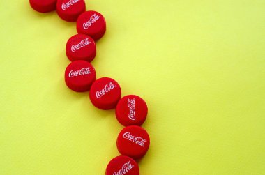 Sarı zemin üzerinde Coca Cola logosu olan bir sürü kırmızı başlık