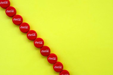 Sarı zemin üzerinde Coca Cola logosu olan bir sürü kırmızı başlık