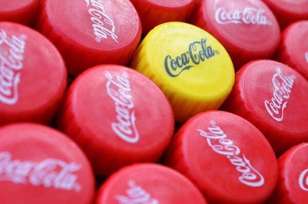 Много красных крышек и один желтый пластиковый колпачок с логотипом кока-колы крупным планом
