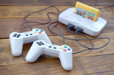 Oyun kartuşu ve tahta arka planda iki oyun kumandası olan eski 8-bit video oyun konsolu