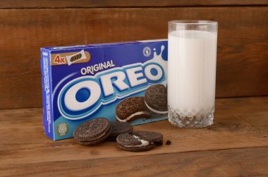 Bir sürü Oreo sandviçi kremalı bisküvi ve tahta arka planda süt bardağı.