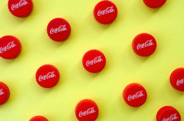 Sarı zemin üzerinde Coca Cola logosu olan bir sürü kırmızı başlık