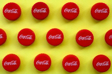 Sarı zemin üzerinde Coca Cola logosu olan bir sürü kırmızı başlık