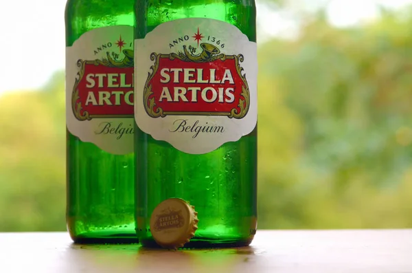 Flaschen stella artois Bier auf verschwommenem grünen Baumhintergrund — Stockfoto