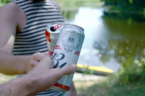 Junger Mann züchtet mit Freund Budweiser Knospenbierdose auf verschwommenem Fluss mit Kajak und Bäumen — Stockfoto