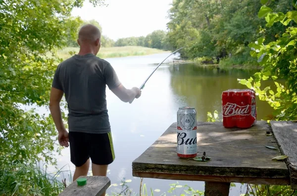 Budweiser Knospe Bierdosen packen auf altem Tisch und Fischer am Fluss im Hintergrund — Stockfoto