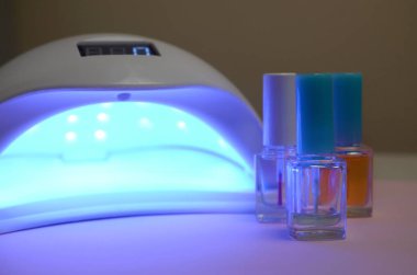 Tırnaklar için UV diyot lambaları ve manikür için kozmetik oje seti ve pastel arka planda pedikür.
