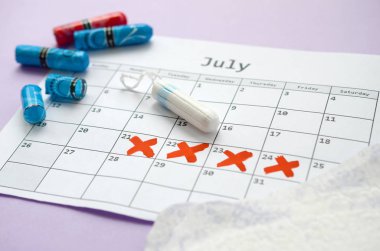 Menstrual pads and tampons on menstruation period calendar with red cross marks lies on lilac background clipart