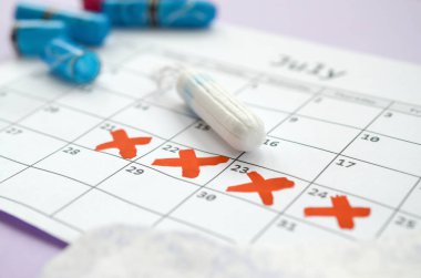 Adet takvimindeki regl pedleri ve tamponlar leylak arka planında kırmızı haç işaretli.