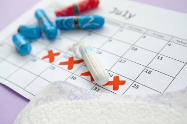 Adet takvimindeki regl pedleri ve tamponlar leylak arka planında kırmızı haç işaretli.