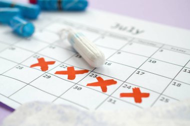 Adet takvimindeki regl pedleri ve tamponlar leylak arka planında kırmızı haç işaretli.