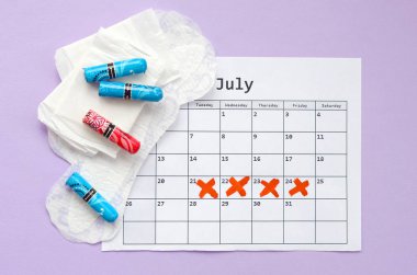 Menstrual pads and tampons on menstruation period calendar flat lay on lilac background clipart