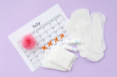 Menstrual pads and tampons on menstruation period calendar flat lay on lilac background clipart