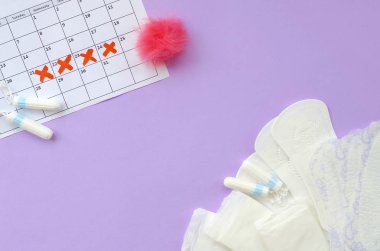 Adet takviminde regl pedleri ve tamponlar leylak arkaplanının üzerinde yatıyordu
