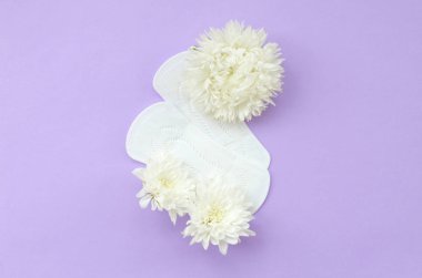 Beyaz çiçekler regl pedlerinin üzerinde uzanır. Pastel eflatun arka planda. Yukardan bakıldığında düz.