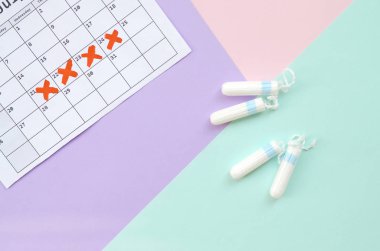 Mavi pembe ve eflatun pastel arka planda takvim ve adet tamponlu düz kompozisyon