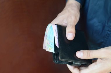 Elinde Ukrayna parası olan siyah deri bir cüzdan ya da para dolu cüzdan çalan bir hırsız var.