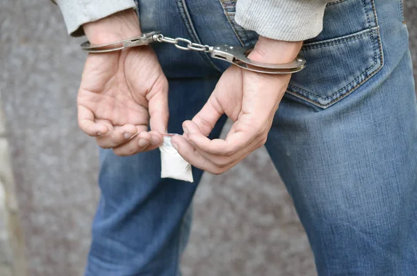 Gearresteerde drugsdealer in handboeien van de politie met kleine heroïne drugspakket op donkere muur achtergrond — Stockfoto
