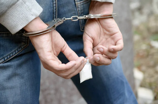 Arresterad knarklangare i polisens handbojor med små heroinpaket på mörk vägg bakgrund — Stockfoto