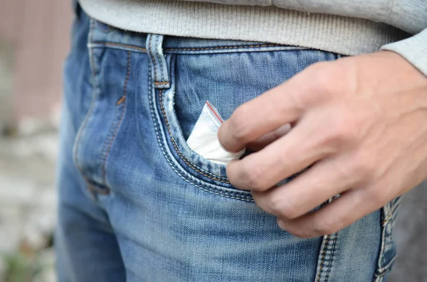 Maschio mano recupero pacchetto di droga il nostro di tasca blu jeans con spazio copia su sfondo edificio abbandonato — Foto Stock