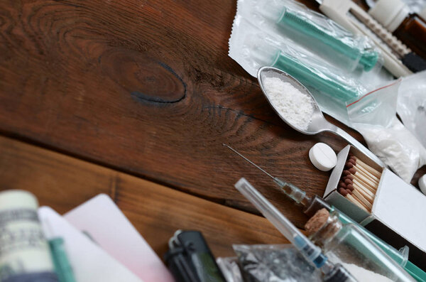 Много наркотических веществ и устройств для приготовления наркотиков лежат на старом деревянном столе
