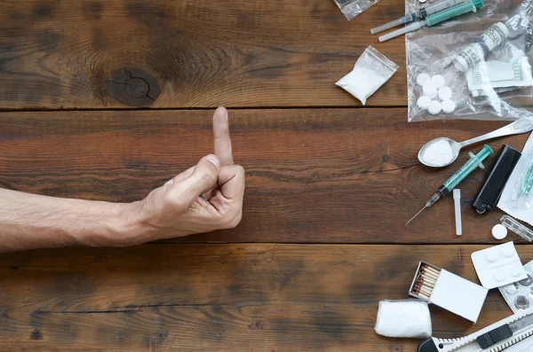 Männliche Hand zeigen fuck Zeichen zu allen Definitionen von Betäubungsmitteln. Viele Medikamententabletten und Pulver auf Holztisch — Stockfoto
