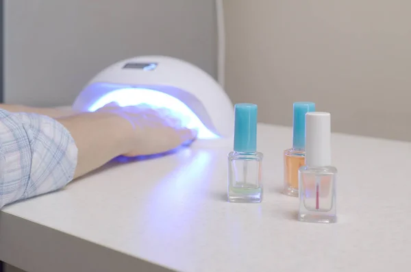 Три бесцветные прозрачные бутылки для лака для ногтей на фоне женских рук в гель UV привели лампы для сушки маникюра — стоковое фото