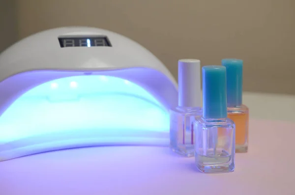 UV diode lamp lights for nails and set of cosmetic nail polish for manicure and pedicure on pastel background