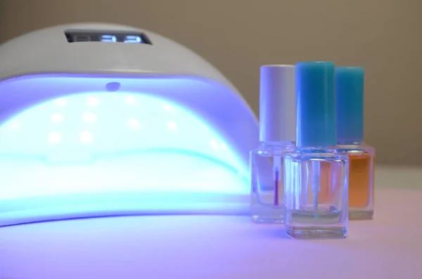 УФ-лампы лампы для ногтей и набор косметического лака для ногтей для маникюра и педикюра на пастельном фоне — стоковое фото