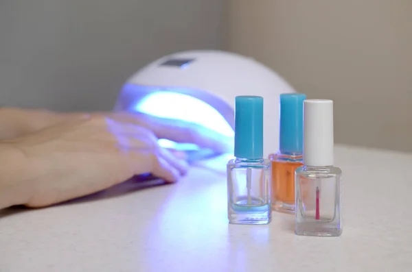 Три бесцветные прозрачные бутылки для лака для ногтей на фоне женских рук в гель UV привели лампы для сушки маникюра — стоковое фото