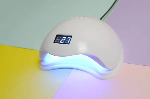 Lâmpada de unha LED UV para processo de cura pelo método de gel encontra-se na mesa multicolorida pastel — Fotografia de Stock